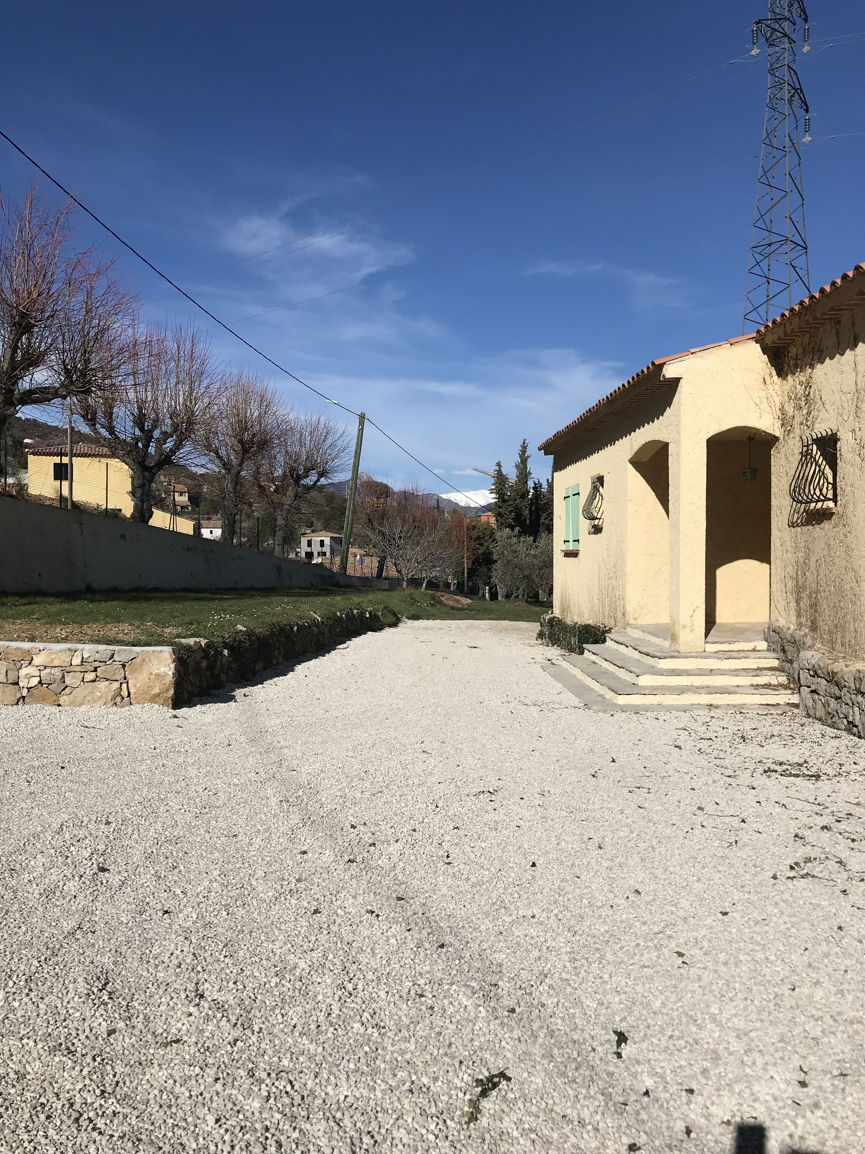 A gravel driveway leading to a building with a tiled roof and a stone wall.