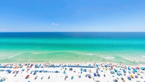 Una playa con numerosos sombrillas y tumbonas, un cielo azul despejado y el océano.