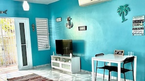 Een woonkamer met een blauwe muur, een witte tv-kast, een eettafel met stoelen en een vloer met een patroon.