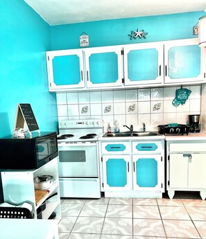 Compact kitchen with white cabinetry, blue accents, and a stove, sink, and refrigerator.