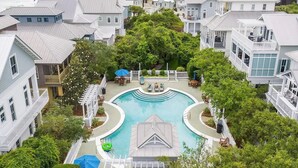 A residential area with a swimming pool surrounded by houses, trees, and outdoor furniture.