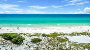 A beach with clear turquoise water, white sand, and sparse vegetation in the foreground.