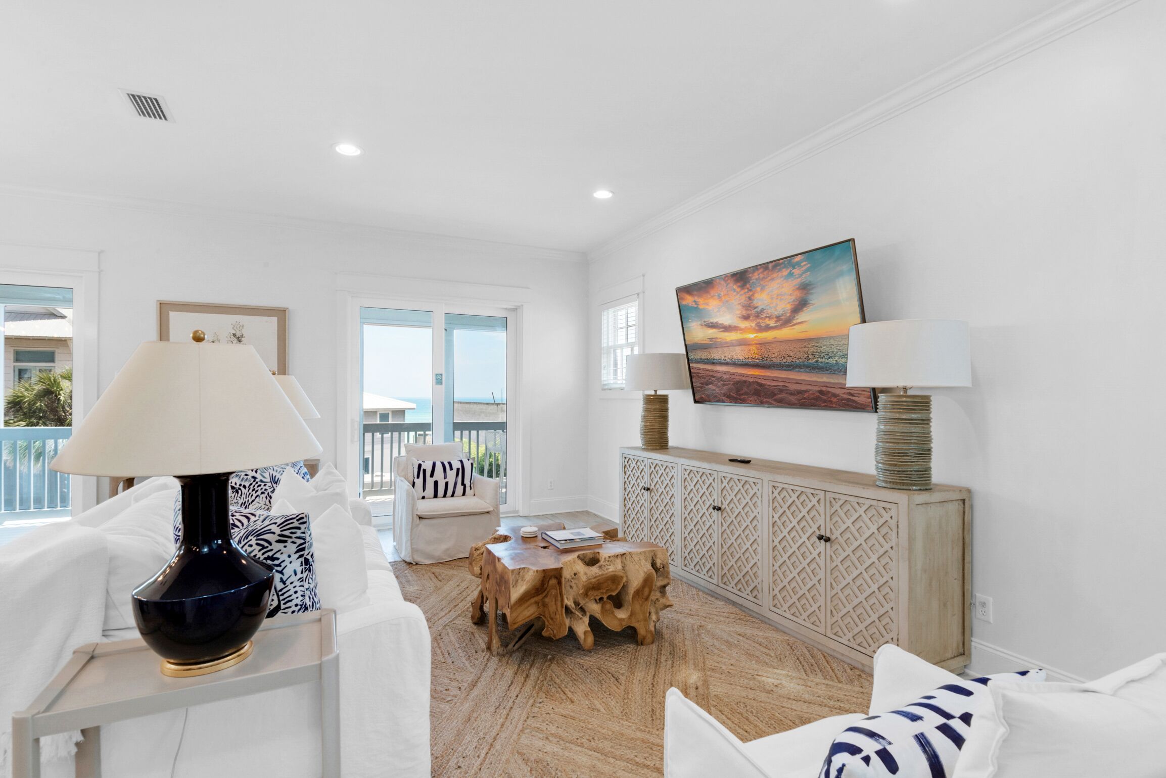 A bright, white living room with a wooden coffee table, a white sofa, and a large painting of a sunset.
