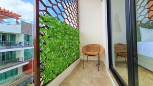 A balcony with a green plant wall, a wicker chair, and a view of a building across the street. - Bahay By Riviera Rentals (Playa del Carmen)