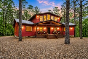 A red wooden cabin with a porch, surrounded by trees.