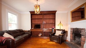 A living room with a fireplace, a leather sofa, a wooden cabinet, and a chandelier. - Heritage Row House beside Citadel Hill (Halifax)