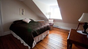 A bedroom with a sloped ceiling, a bed with a dark bedspread, a chair, a small table, and a lamp. - Heritage Row House beside Citadel Hill (Halifax)