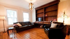 A living room with a wooden floor, a black leather sofa, a wooden cabinet, and a television. - Heritage Row House beside Citadel Hill (Halifax)
