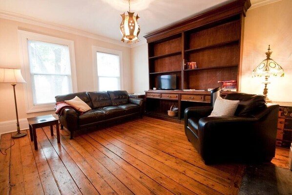 Un salon avec un plancher en bois, un canapé en cuir noir, un meuble en bois et un téléviseur.