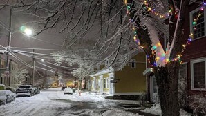 Eine verschneite Straße mit Häusern an beiden Seiten, verziert mit bunten Lichtern.