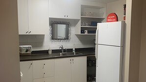 Une cuisine avec des meubles blancs, un plan de travail noir, un four encastré et un réfrigérateur.