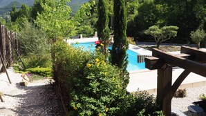 Zona de piscina con montañas al fondo, rodeada de vegetación y una terraza de madera.