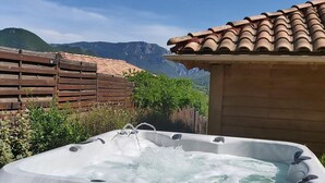 Un jacuzzi con un banco de madera al frente, rodeado por una valla de madera y follaje, con una vista de montaña al fondo.