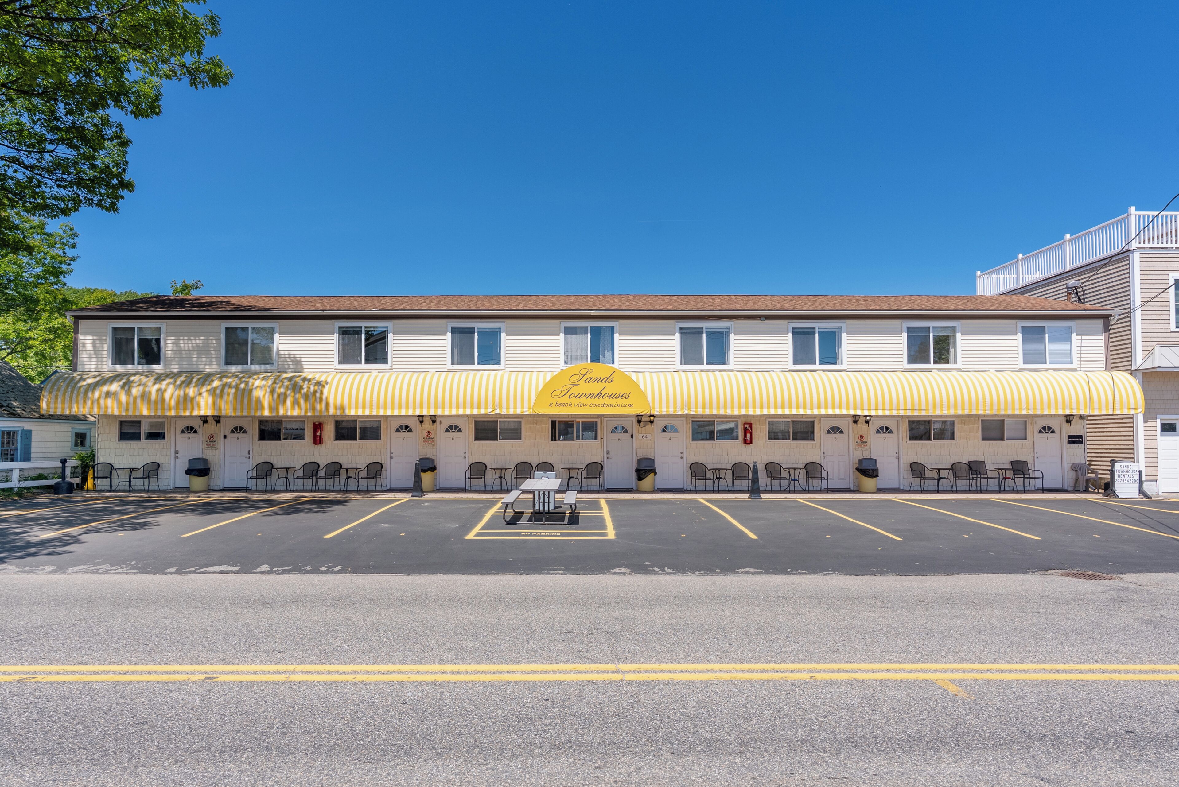 A motel with a yellow awning, outdoor seating, and a parking lot.