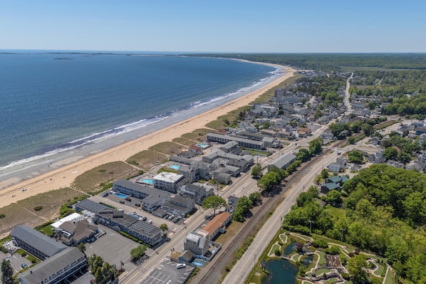 Vista aérea de un pueblo costero con playa, edificios residenciales y un lago pequeño.