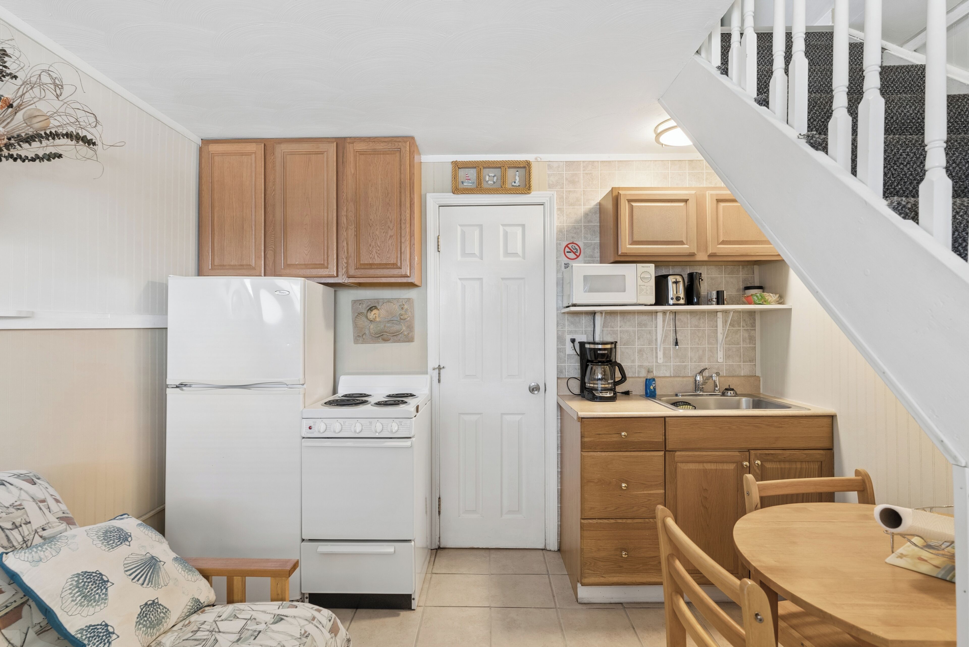 A compact kitchen with wooden cabinets, a white refrigerator, a stove, a microwave, and a sink.