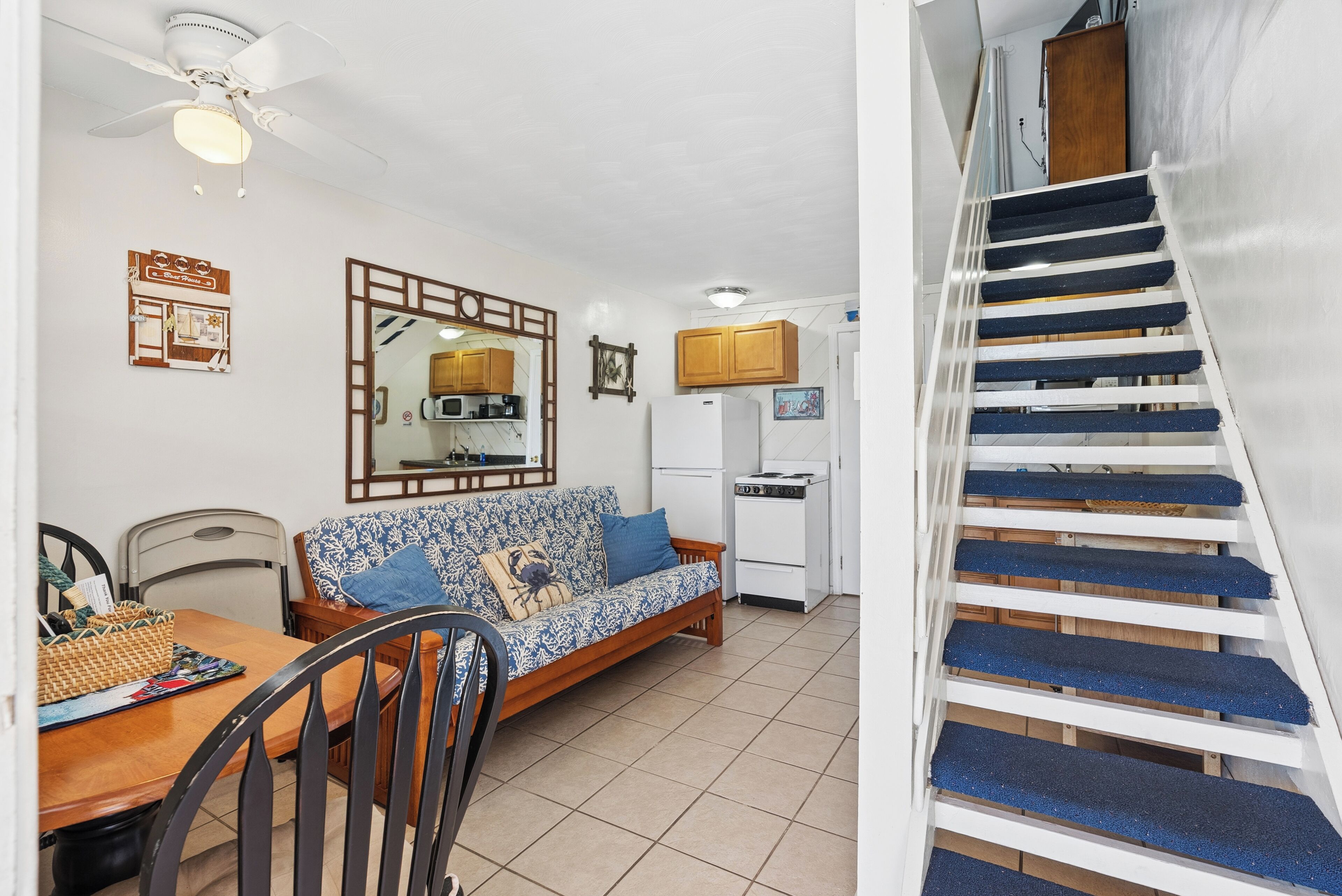 A compact living space with a sofa, dining table, chairs, a ceiling fan, a microwave, a refrigerator, and a staircase.