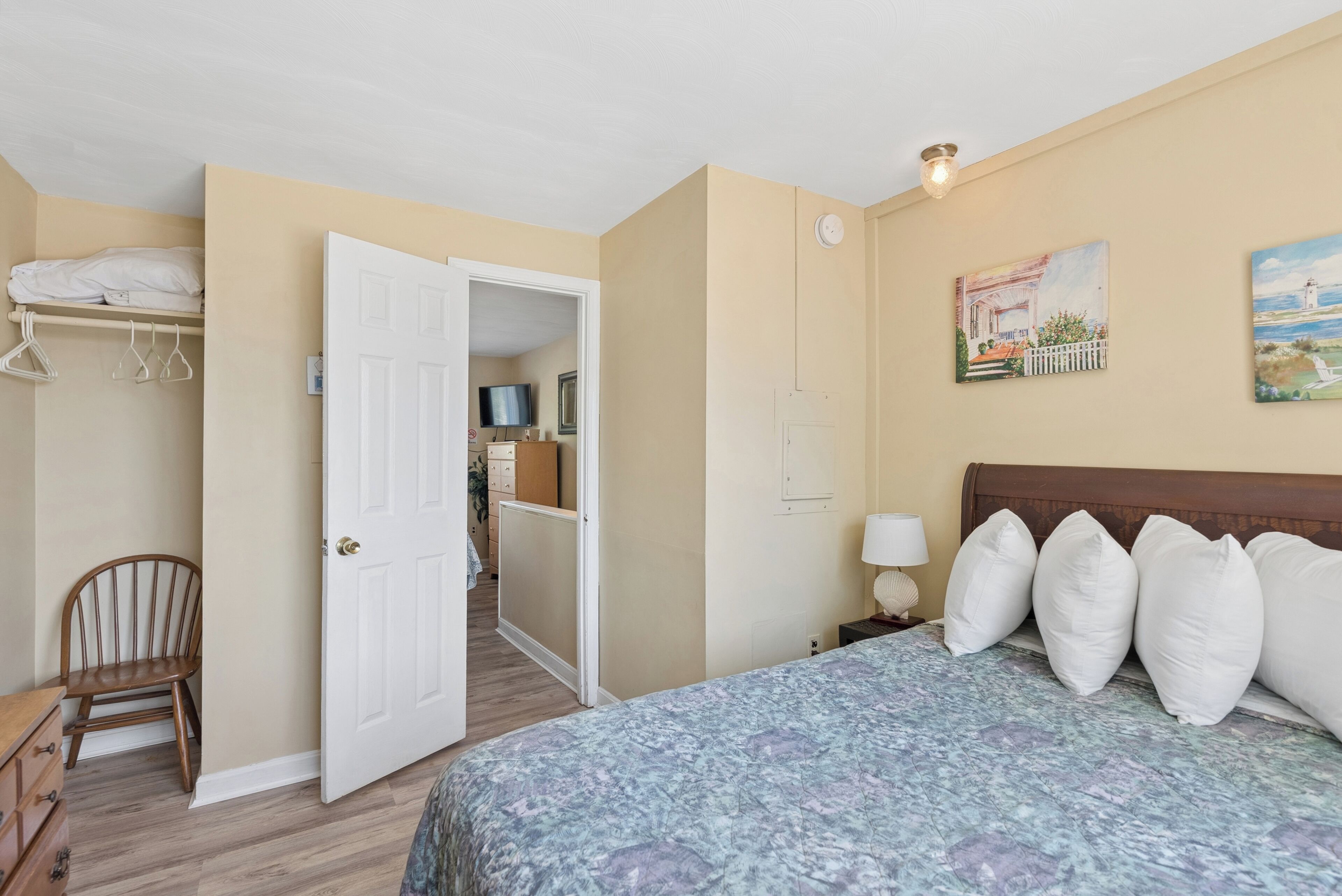 Une chambre à coucher comprenant un lit, une chaise, une armoire et une porte donnant sur une autre pièce.