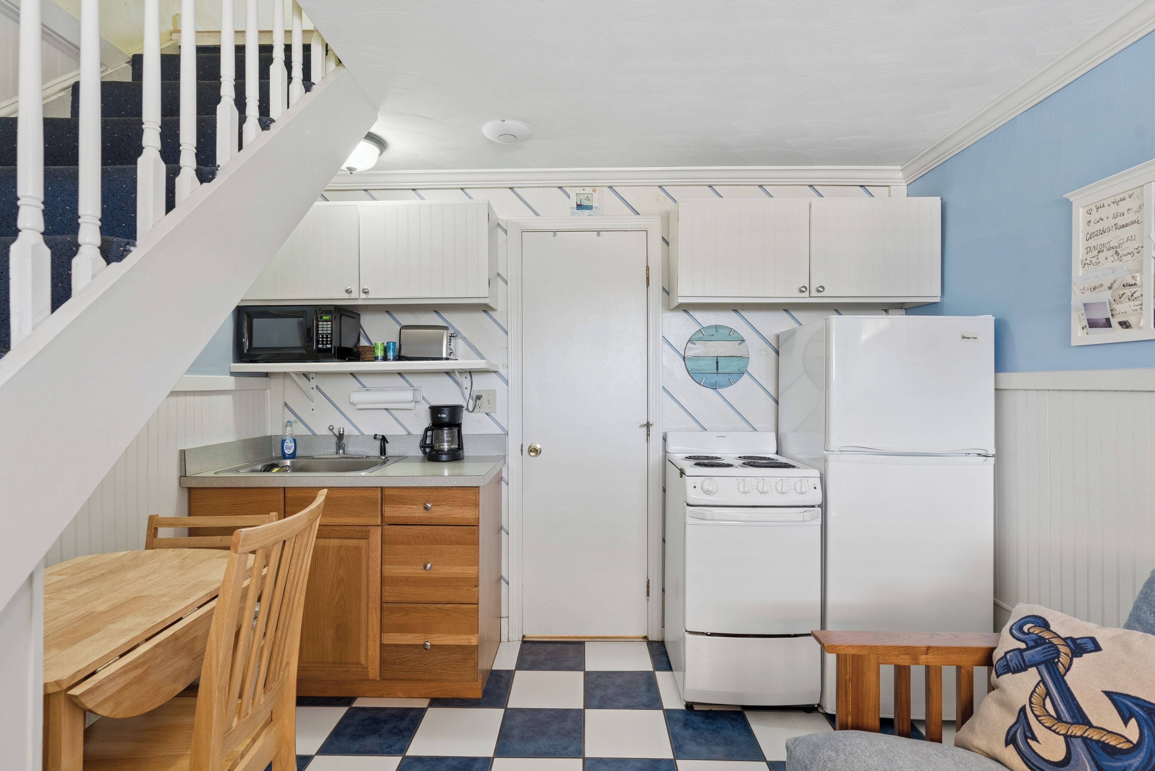 Une cuisine avec des meubles blancs, un four à micro-ondes, une cuisinière et un réfrigérateur. On y trouve une table et des chaises en bois, ainsi qu'un sol à carreaux.