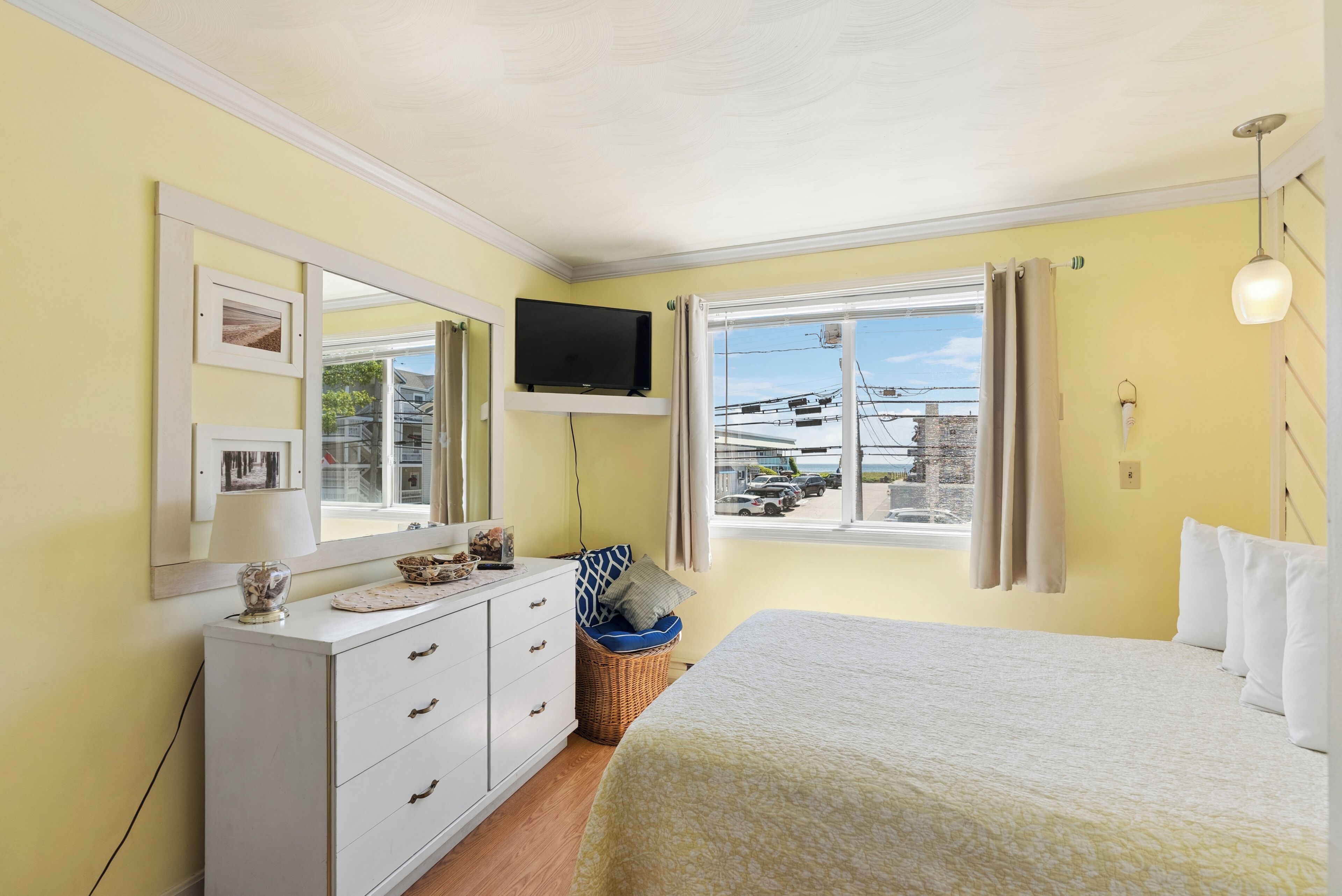 A bedroom with a bed, a dresser, a television, and a window with a view of the outside.
