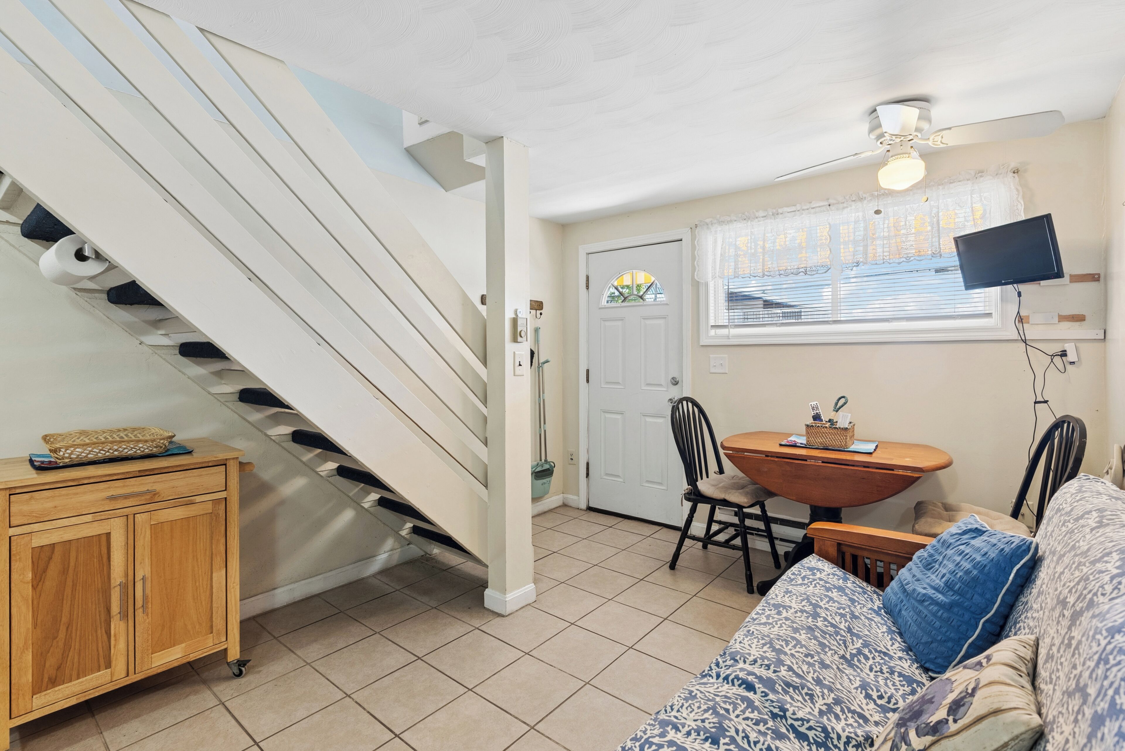 A staircase leading to a door, a dining table with chairs, a sofa, and a television mounted on the wall.