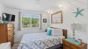 A bedroom with a bed, a dresser, a TV, a window with a view, and a starfish decoration. - Sands Townhouses (Old Orchard Beach)