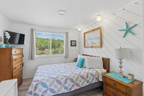 Un dormitorio con cama, cómoda, televisor, ventana con vistas y decoración de estrella de mar.