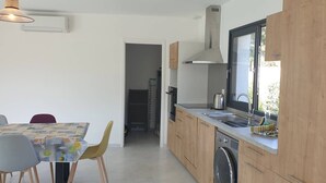 A modern kitchen with wooden cabinets, a built-in oven, and a dishwasher. There is a dining area with a table and chairs. - Villa Rossa, 6 pers dans résidence avec piscine chauffée privée (Lecci)