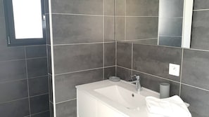 A modern bathroom with dark tiles, a white sink, a mirror, and a towel.