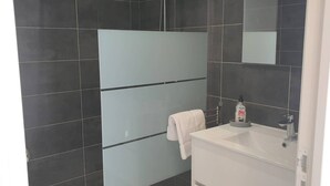 A modern bathroom with dark tiles, a glass shower enclosure, a white sink, and a towel hanging on a rack. - Villa Rossa, 6 pers dans résidence avec piscine chauffée privée (Lecci)