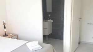 A hotel room with a bed, a bedside table with a lamp, a bathroom with a shower, and a door leading to another room. - Villa Rossa, 6 pers dans résidence avec piscine chauffée privée (Lecci)