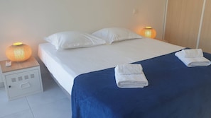 A neatly made bed with white linens and a blue bedspread, two white pillows, and two folded towels on the bed.