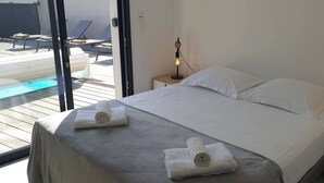 A bedroom with a bed, two rolled towels, a nightstand with a lamp, and a view of an outdoor pool area. - Villa Rossa, 6 pers dans résidence avec piscine chauffée privée (Lecci)