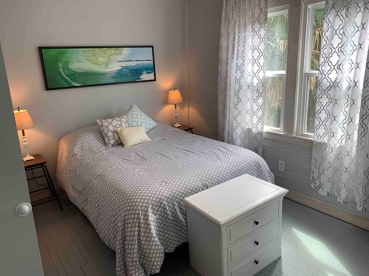 A neatly arranged bedroom with a bed, bedside tables, a nightstand, a lamp, and a window with curtains.