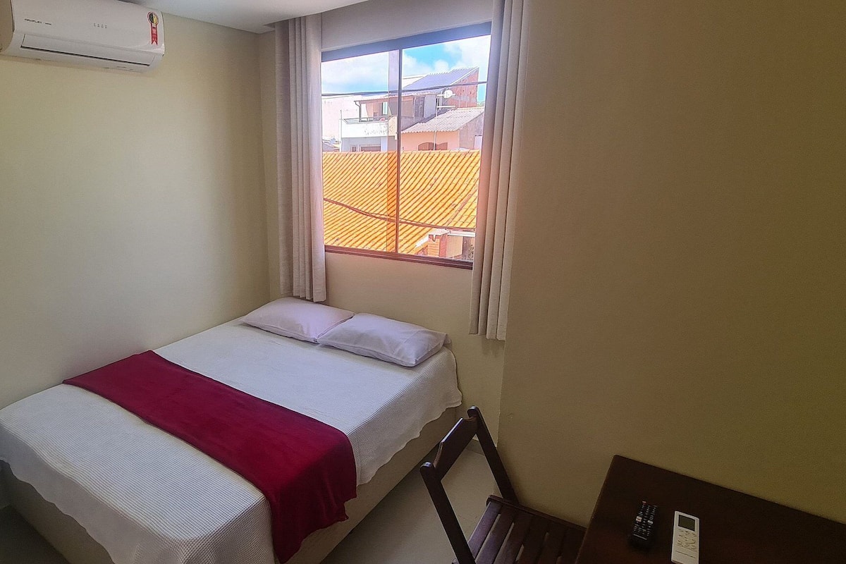 Ein kleines Zimmer mit einem Einzelbett, einem Fenster, einem Heizkörper und einem kleinen weißen Gerät.