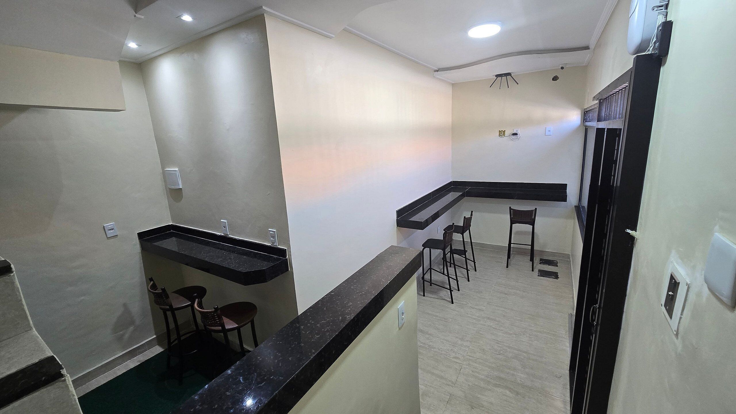 A modern kitchen with a black countertop, a built-in sink, and a small dining area with two stools.