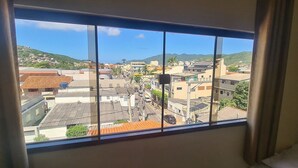 A room with a large window overlooking a town with buildings and hills.