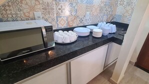A kitchen with a microwave, stacked plates, and cups on the counter. - Recanto Del Mare (Arraial do Cabo)