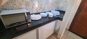 A kitchen with a microwave, stacked plates, and cups on the counter.