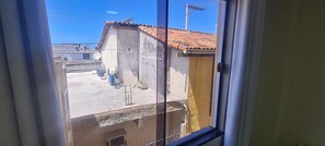 A view through a window of a building with a tiled roof, a satellite dish, and a concrete wall. - Recanto Del Mare (Arraial do Cabo)