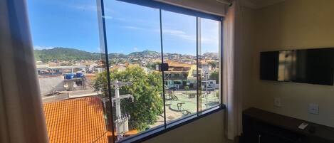 A room with a large window offering a view of a town with buildings and a hill.