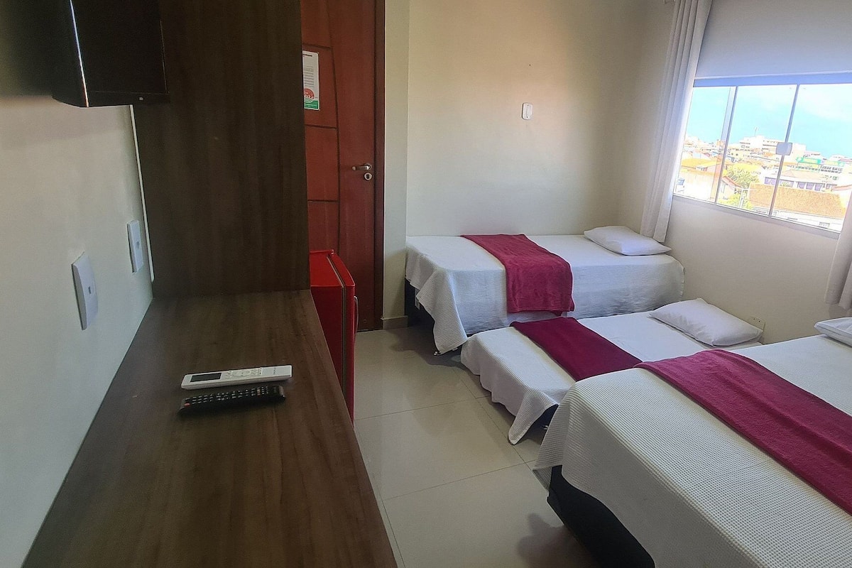 Ein Hotelzimmer mit zwei Betten, einem Holztisch, einer Fernbedienung und einem Fenster mit Blick auf die Stadt.