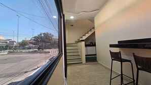 A hotel room with a view of the street, a staircase leading to the kitchen, and two bar stools. - Recanto Del Mare (Arraial do Cabo)