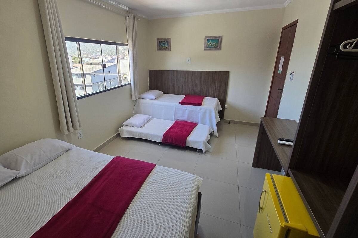 A hotel room with two beds, a window with curtains, a wooden headboard, and a small table.