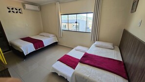 A room with two single beds, a window with curtains, an air conditioning unit, and a view of buildings outside. - Recanto Del Mare (Arraial do Cabo)