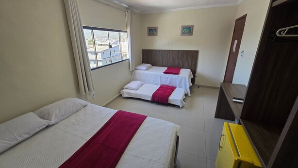 A hotel room with two beds, a window with curtains, a wooden headboard, and a small table.