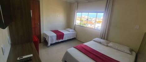 Una habitación de hotel con dos camas, televisión, ventana con vista a la ciudad y una puerta.