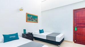 Una habitaci ón de hotel con dos camas, una mesita de noche, un cuadro en la pared y una puerta de madera.
