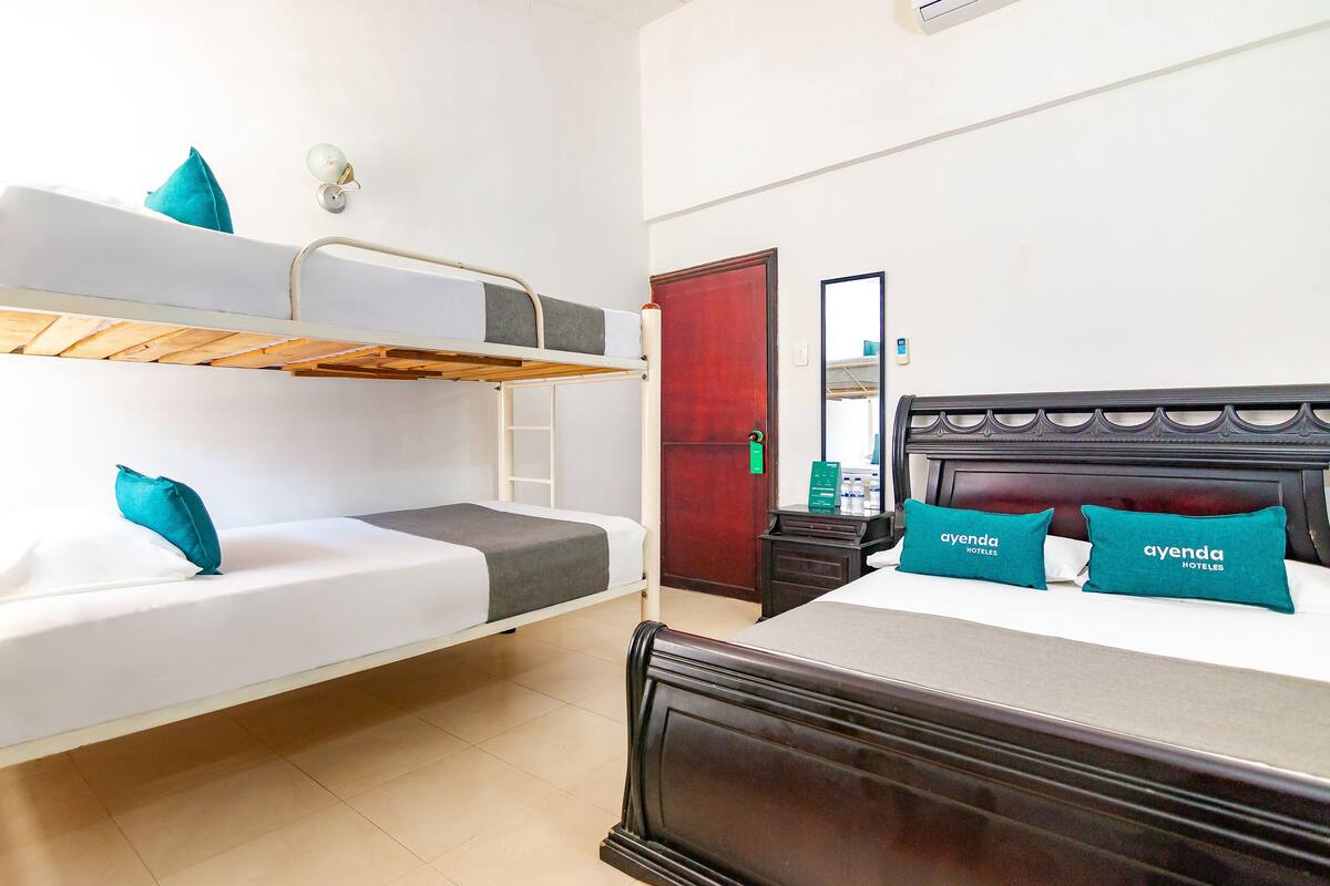 Habitación de hotel con literas, una cama individual con cabecera y una mesita de noche pequeña con artículos de aseo.