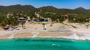 A beachfront property with a pool, palm trees, and a mountain backdrop.